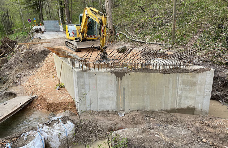 Auffüllen der Stützwand nach der Betonage. Der Bach wurde mit Hilfe von Rohren und befüllten Big-Bags vom neuen Bauwerk ferngehalten.